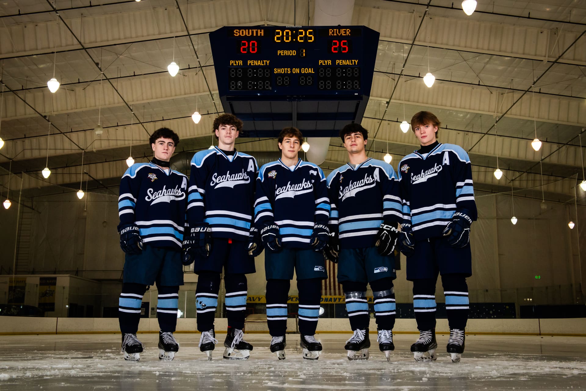 Five South River captains standing on the ice under the rink scoreboard